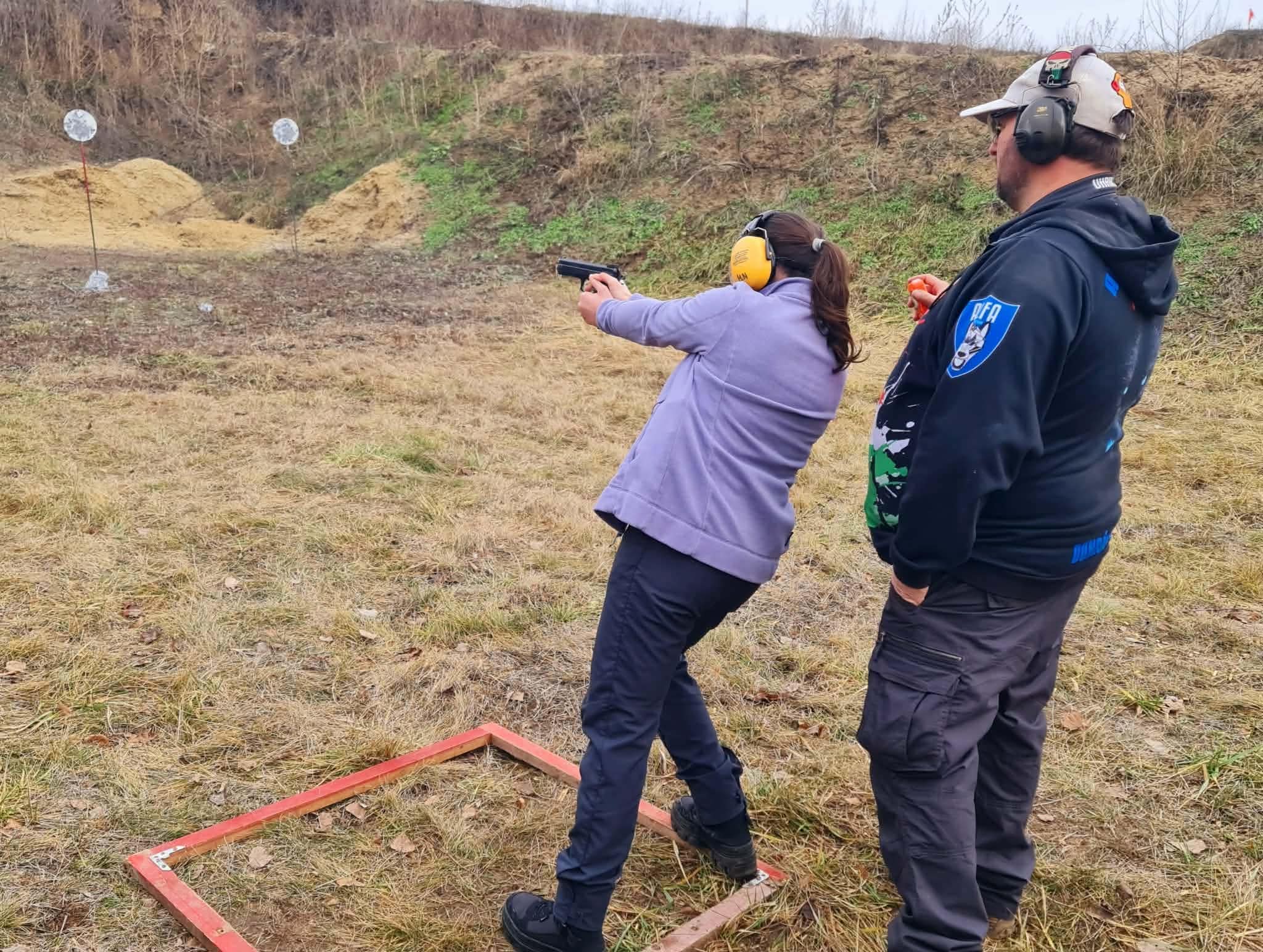 Lövészetvezető egy pisztollyal lövő mellett